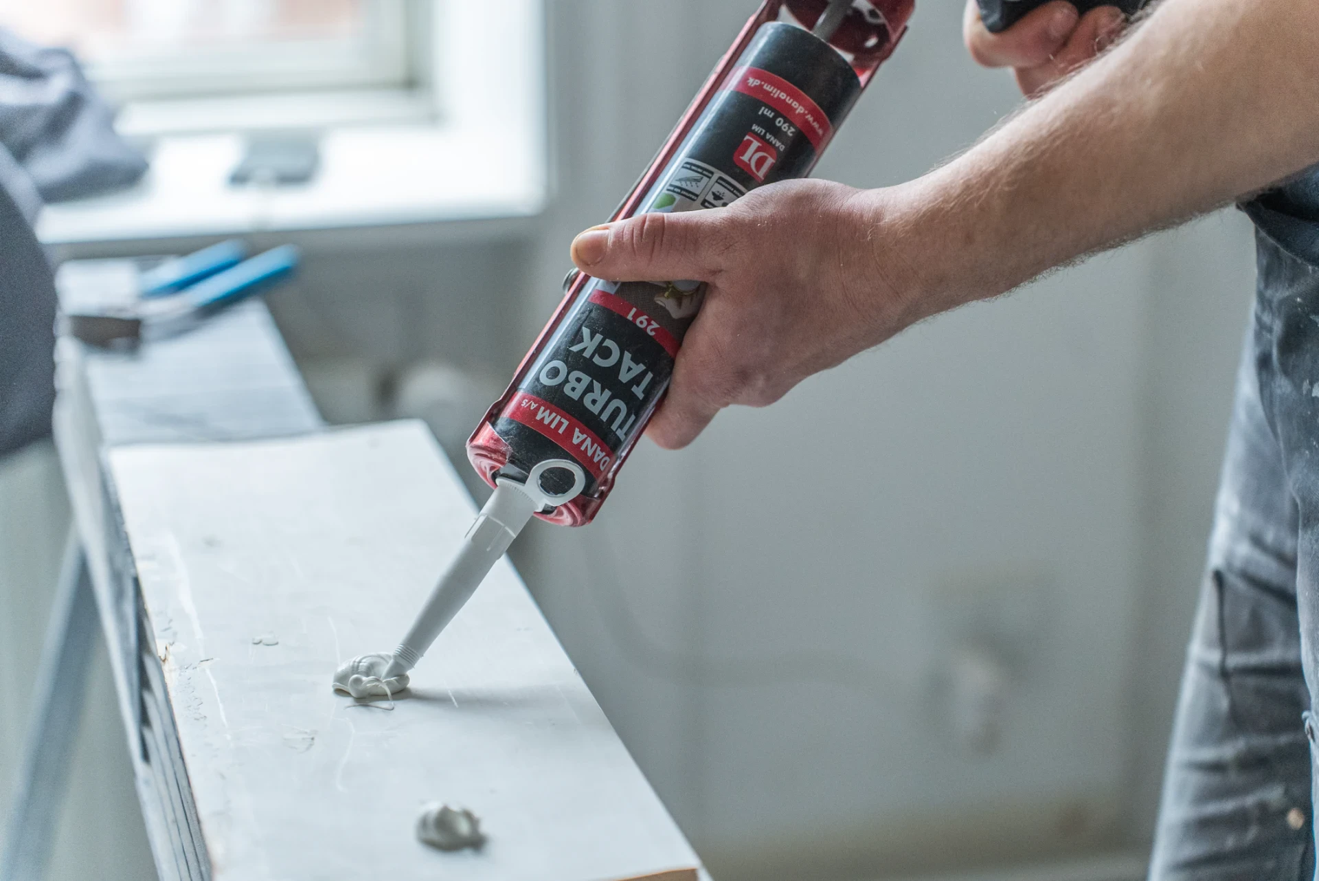 Person påfører silikonefugemasse på væg med en caulkingpistol.