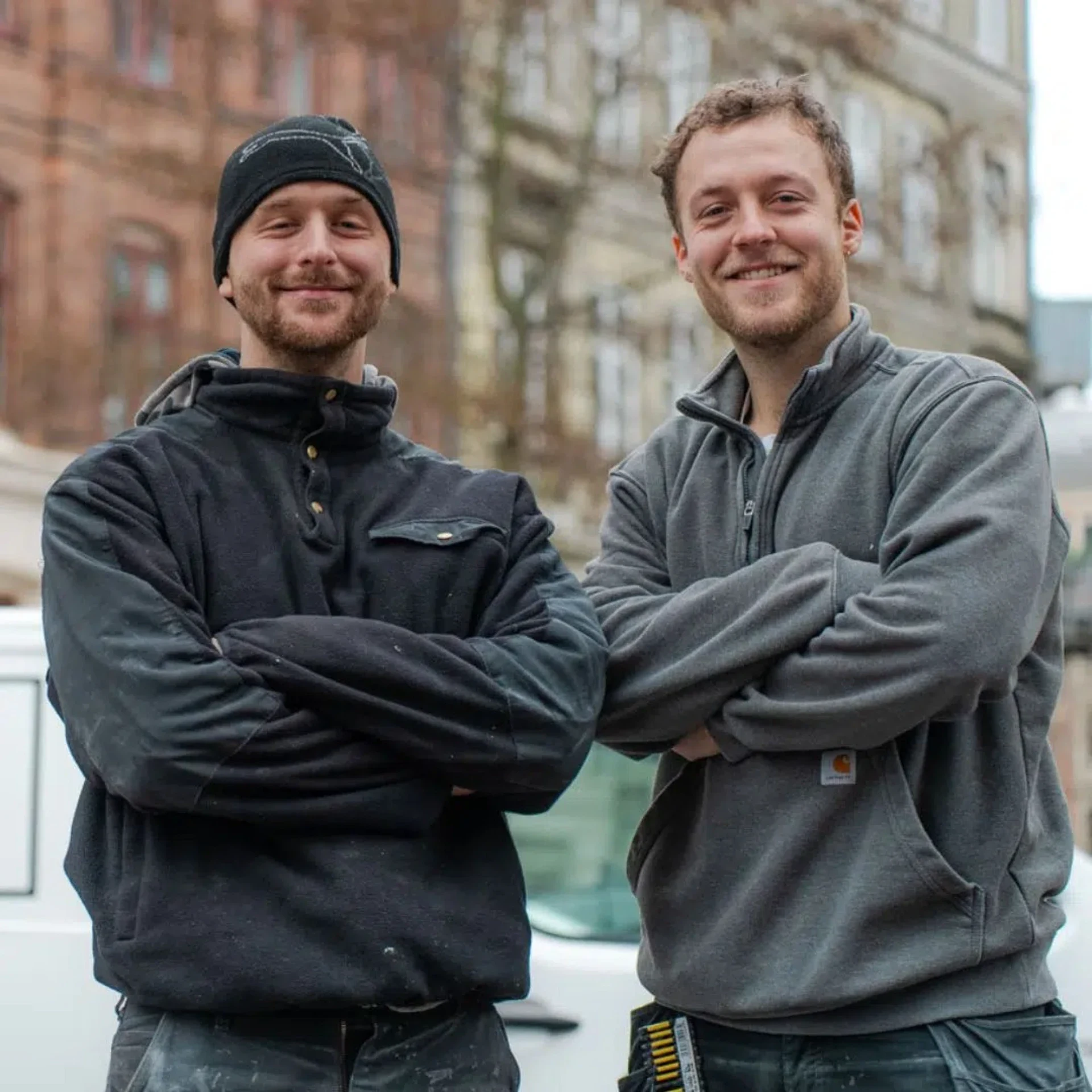Byggefirma med to glade mænd foran en bygning.