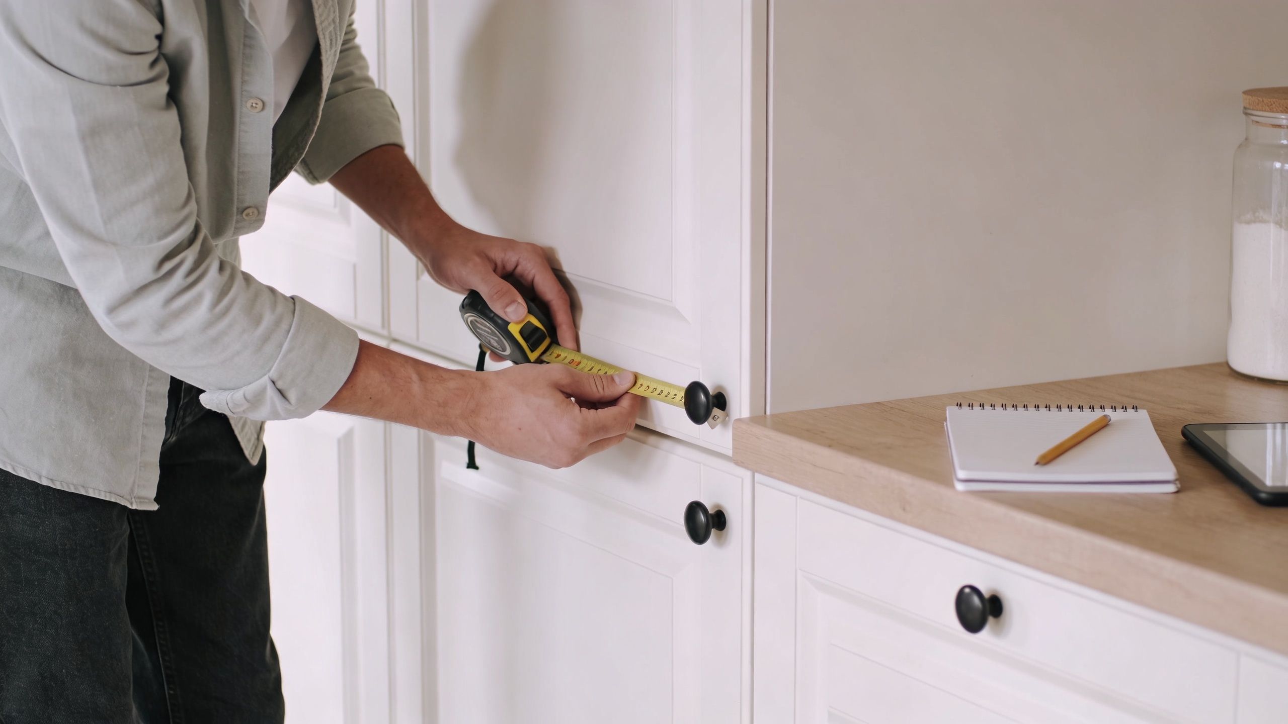 En mand måler en hvid køkkenlåge med et målebånd for at få præcise mål til køkkenrenovering.