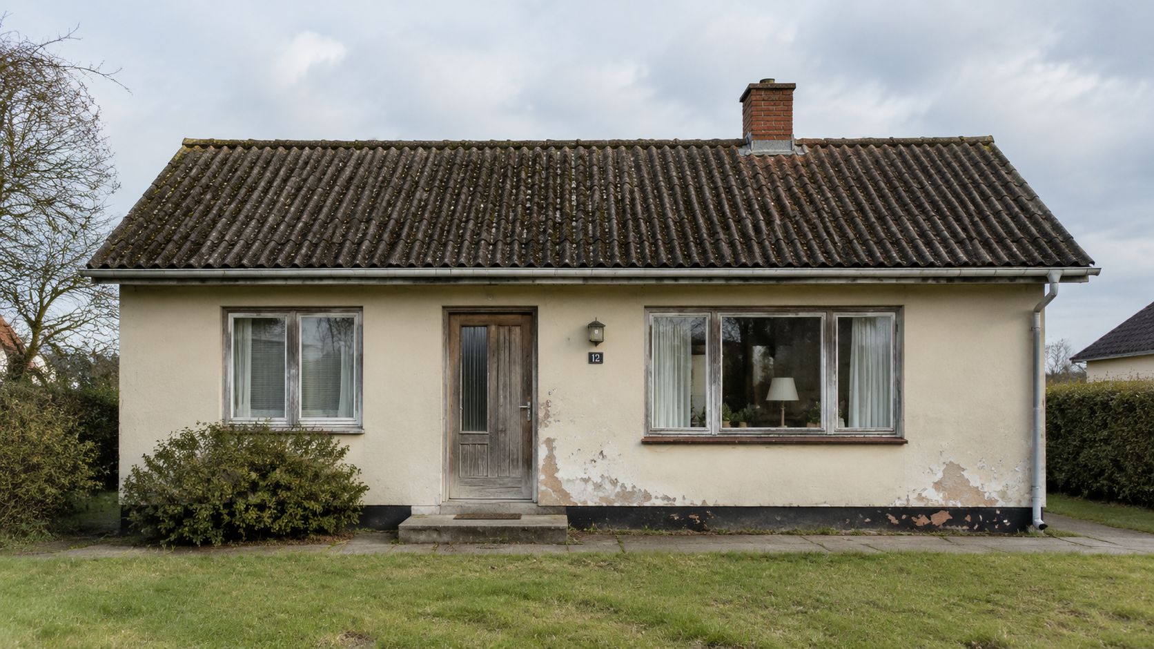 Et ældre parcelhus fra 1970'erne med en slidt facade, der trænger til en grundig udvendig renovering.